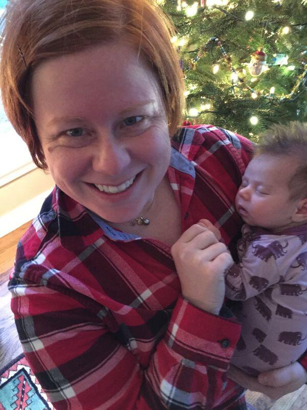 Adoptive parents Rachel holding an infant in front of the Christmas tree