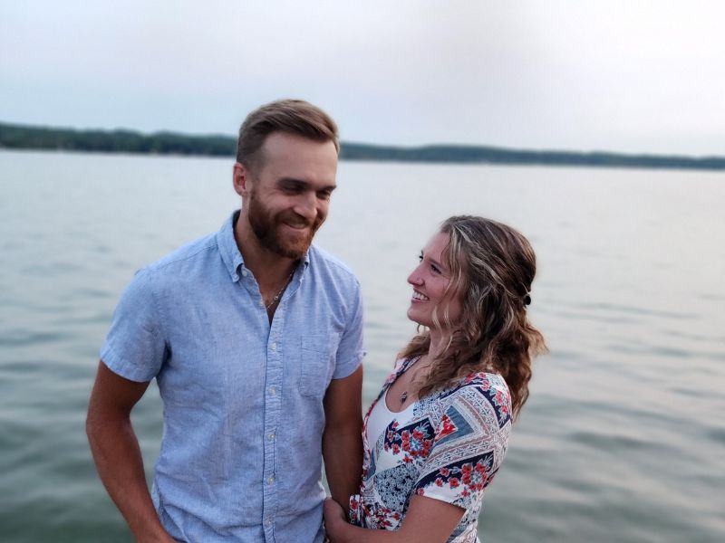 Adoptive couple standing in front of the lake, with mom turned to dad and smiling at him