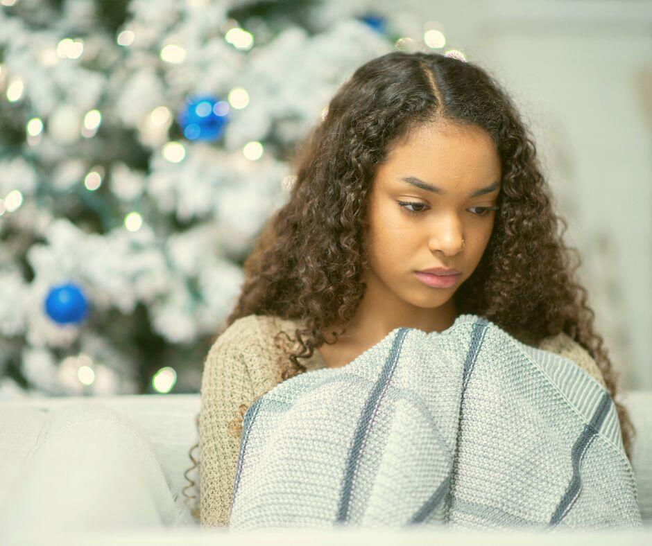 Biracial adopted girl expressing grief in front of a Christmas tree