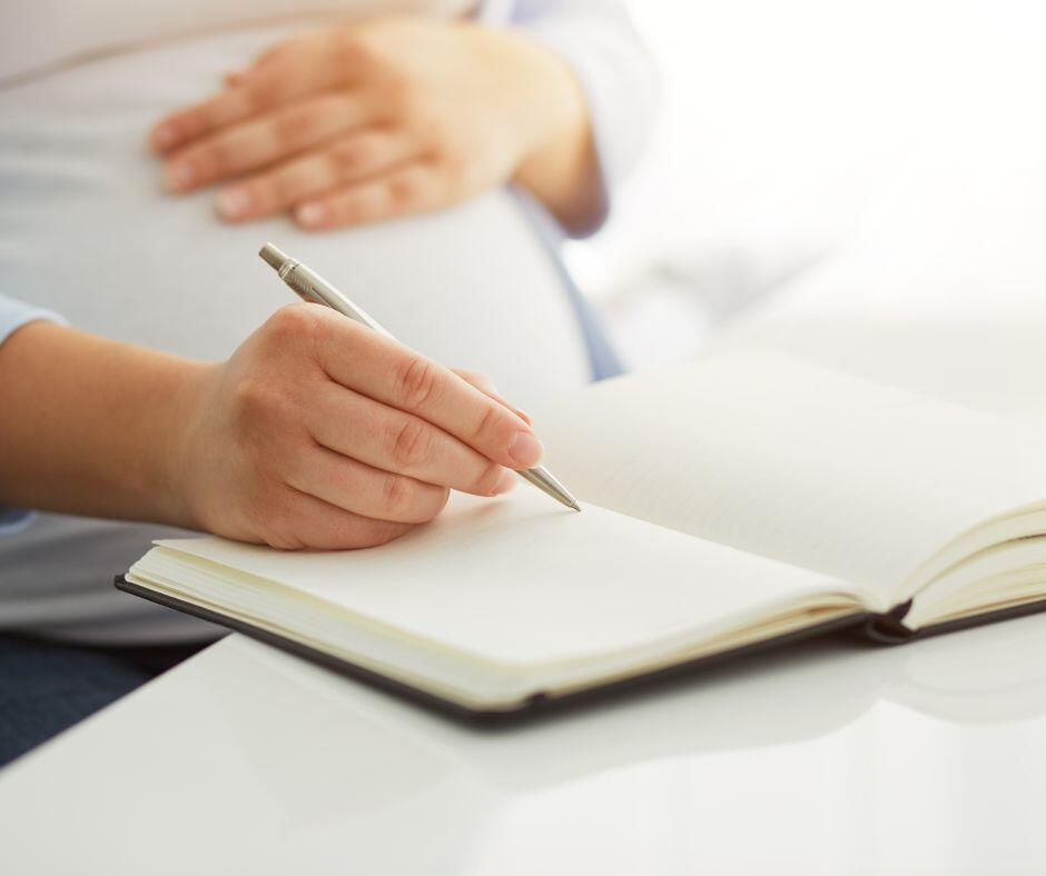 Pregnant woman writing modern adoption plan in a journal